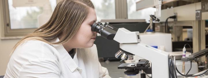 Biology student examining a slide sample on a lab microscope.